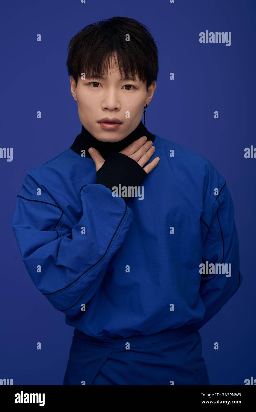 Un giovane uomo asiatico dall'aspetto gradevole posa con grazia con un'espressione accattivante in un blu vivace. Foto Stock