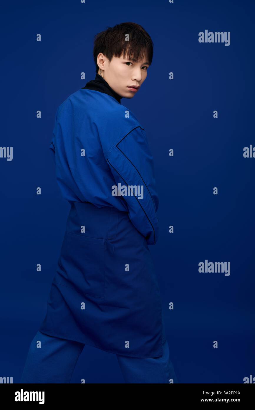 Un giovane uomo sicuro di sé con un abbigliamento blu posa artisticamente su uno sfondo vibrante. Foto Stock