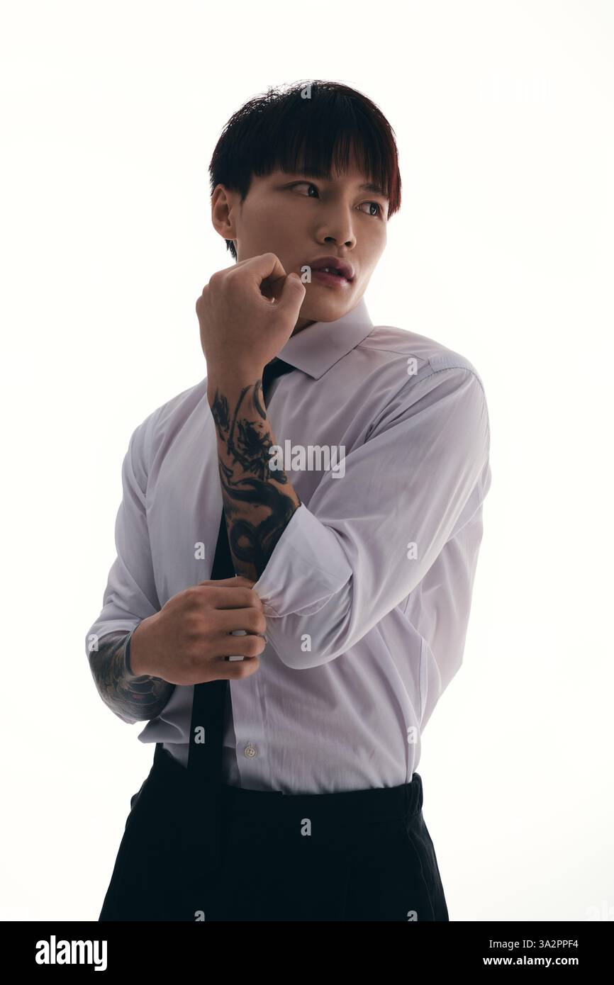 Un giovane asiatico si toglie la manica della camicia, rivelando intricati tatuaggi sotto le luci accese. Foto Stock