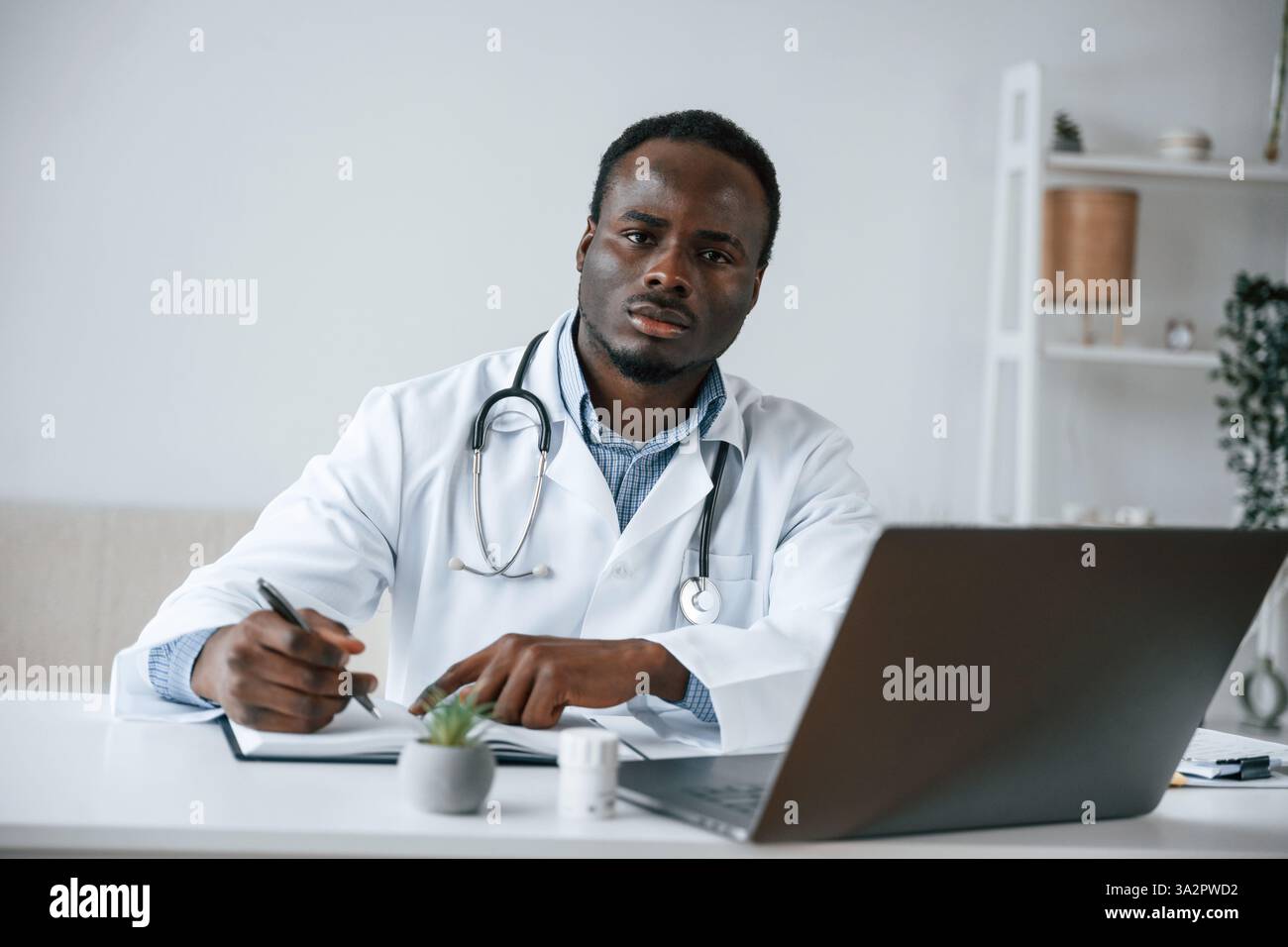 Scrivere le informazioni nel documento. Uomo nero come medico nell'ufficio della clinica. Foto Stock