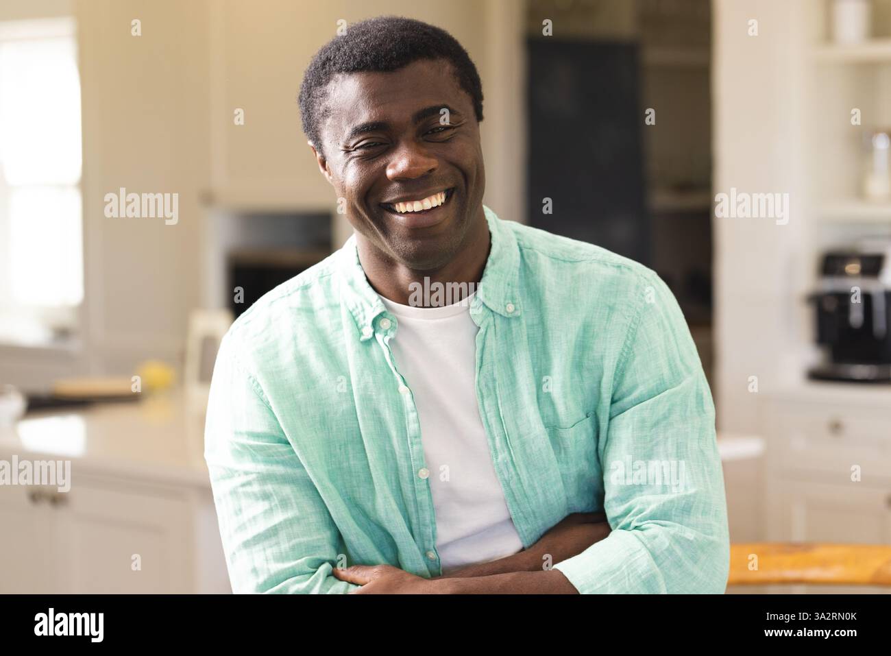 Sorridente uomo afroamericano in cucina che indossa una camicia casual, godendosi un momento di relax a casa Foto Stock Sorridente uomo afroamericano in cucina che indossa una camicia casual, godendosi un momento di relax a casa Foto Stock