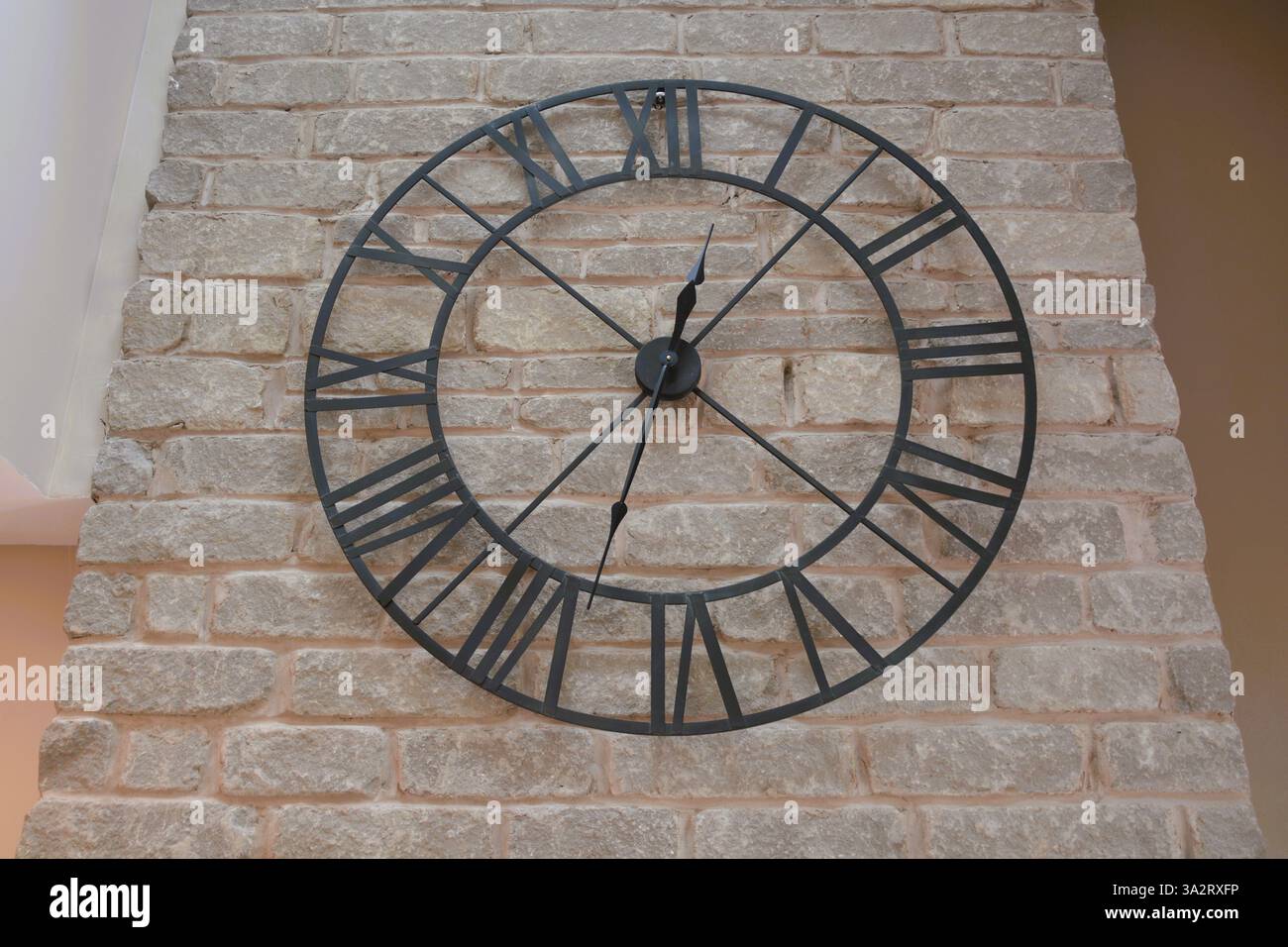 Un grande orologio con struttura metallica con numeri romani è appeso a una parete di pietra grigia. Foto Stock