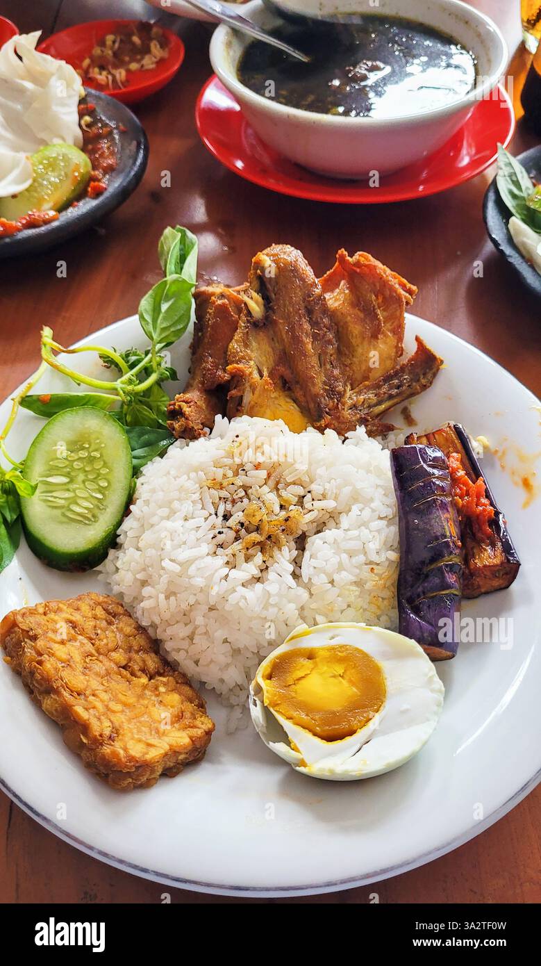 Cibo giavanese orientale Ayam Penyet con melanzane e sambal di peperoncino rosso, tempeh fritto e uovo d'anatra bollito. Foto Stock