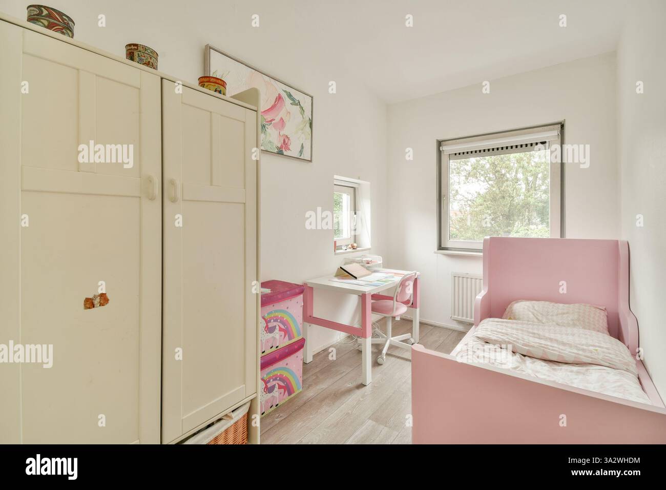 Camera per bambini luminosa e minimalista con letto rosa, mobili bianchi e un'atmosfera allegra perfetta per il relax e la creatività. Foto Stock