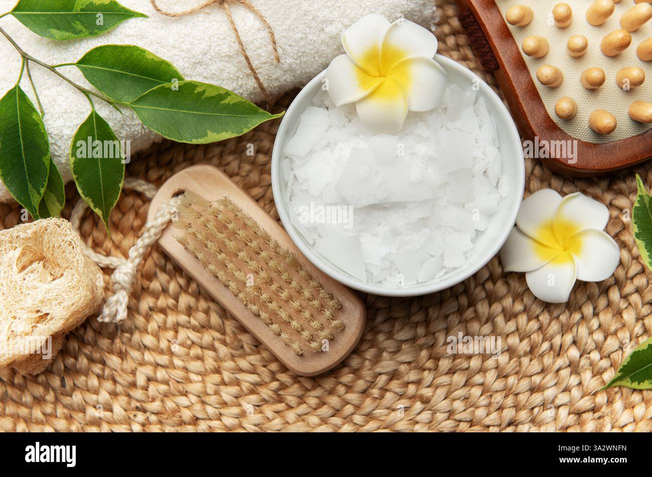 Ambiente benessere con fiocchi di cloruro di magnesio, asciugamano, loofah, pennello e fiori di frangipani Foto Stock