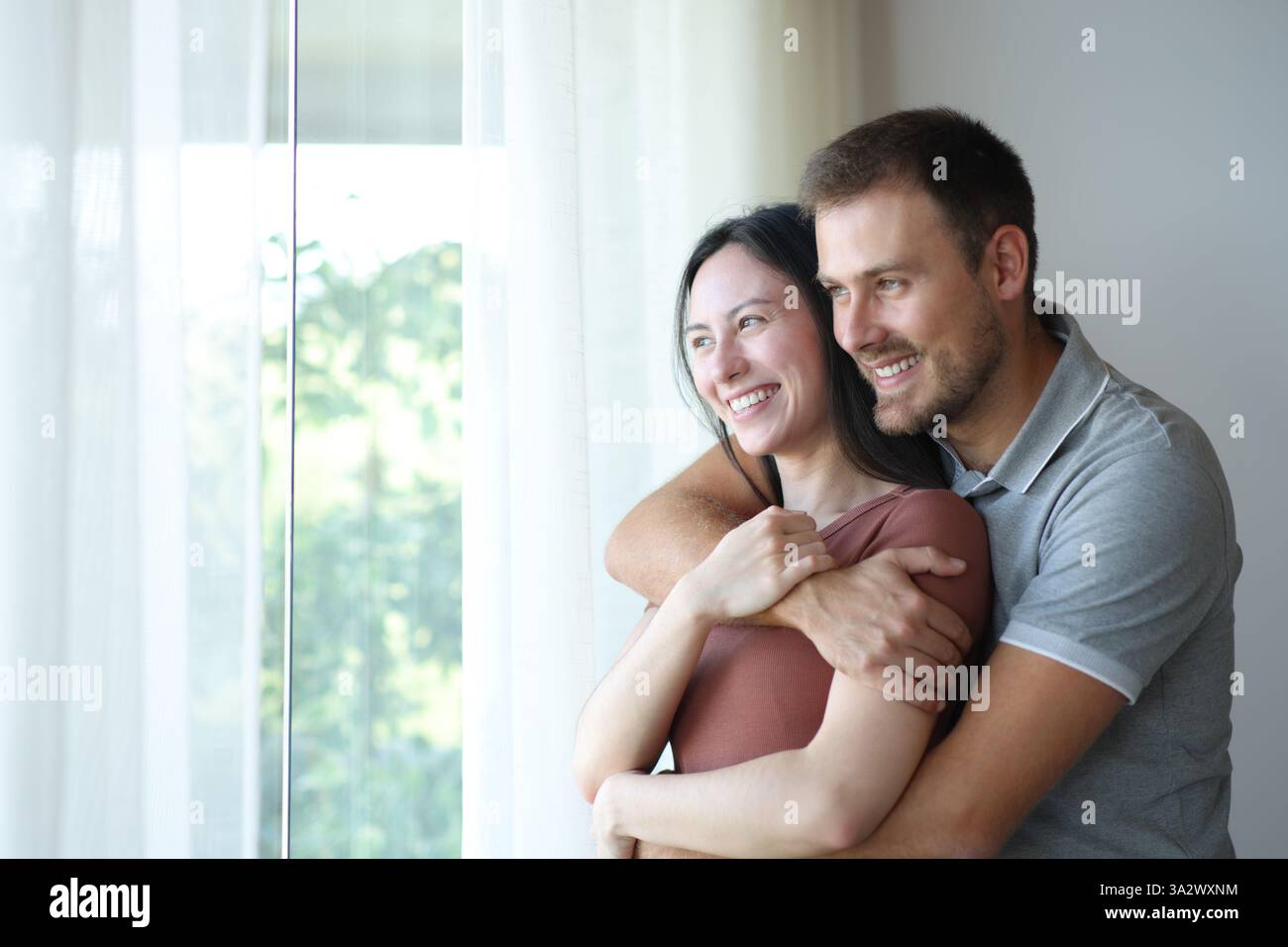 Felice coppia interrazziale che guarda da una finestra a casa Foto Stock