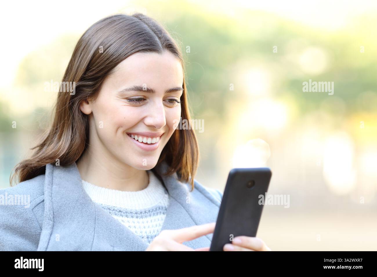 Donna felice che usa il cellulare che cammina in inverno in un parco Foto Stock
