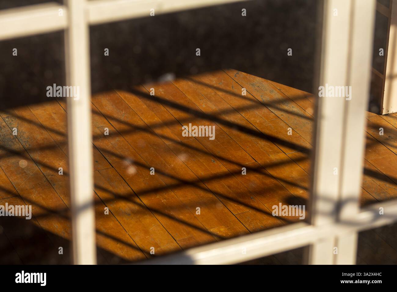 Attraverso una finestra con griglie di legno quadrate, le ombre si allineano perfettamente sul pavimento in legno usurato, creando un motivo ritmico che richiama la finestra Foto Stock