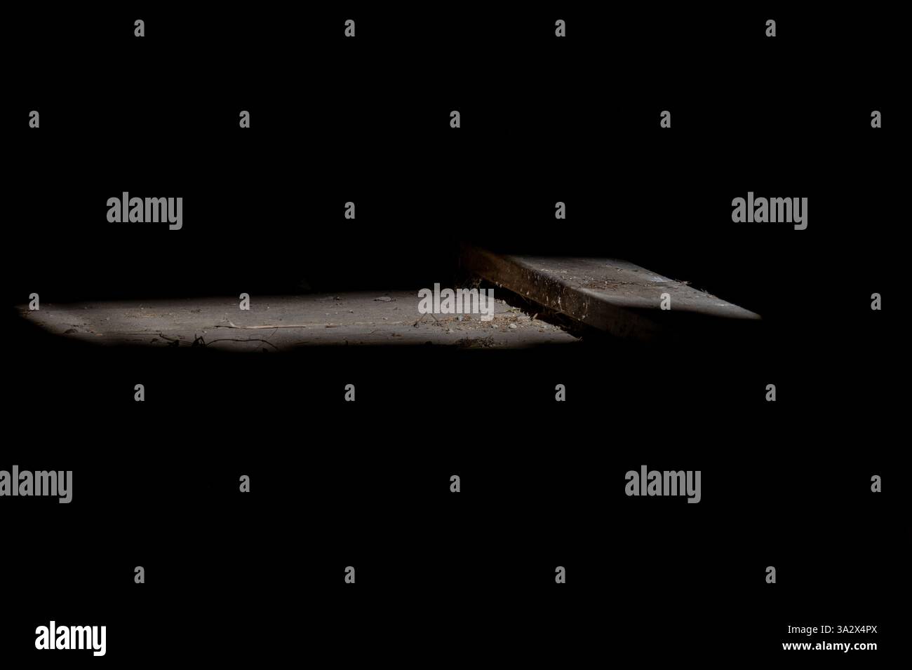 Un suggestivo fascio di luce illumina un pavimento in legno polveroso in una vecchia baracca, rivelando tavole vecchie e sporcizia sparsa, mentre l'ambiente circostante è buio Foto Stock