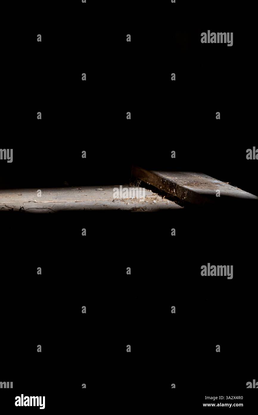 Un suggestivo fascio di luce illumina un pavimento in legno polveroso in una vecchia baracca, rivelando tavole vecchie e sporcizia sparsa, mentre l'ambiente circostante è buio Foto Stock