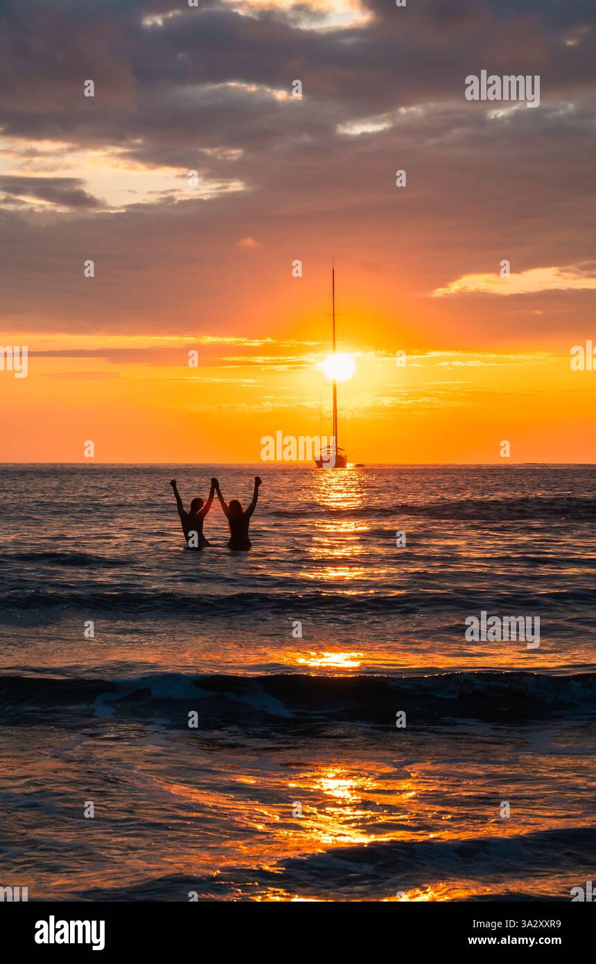 Coppia con le mani in aria guardando il bellissimo tramonto nell'oceano. Foto Stock