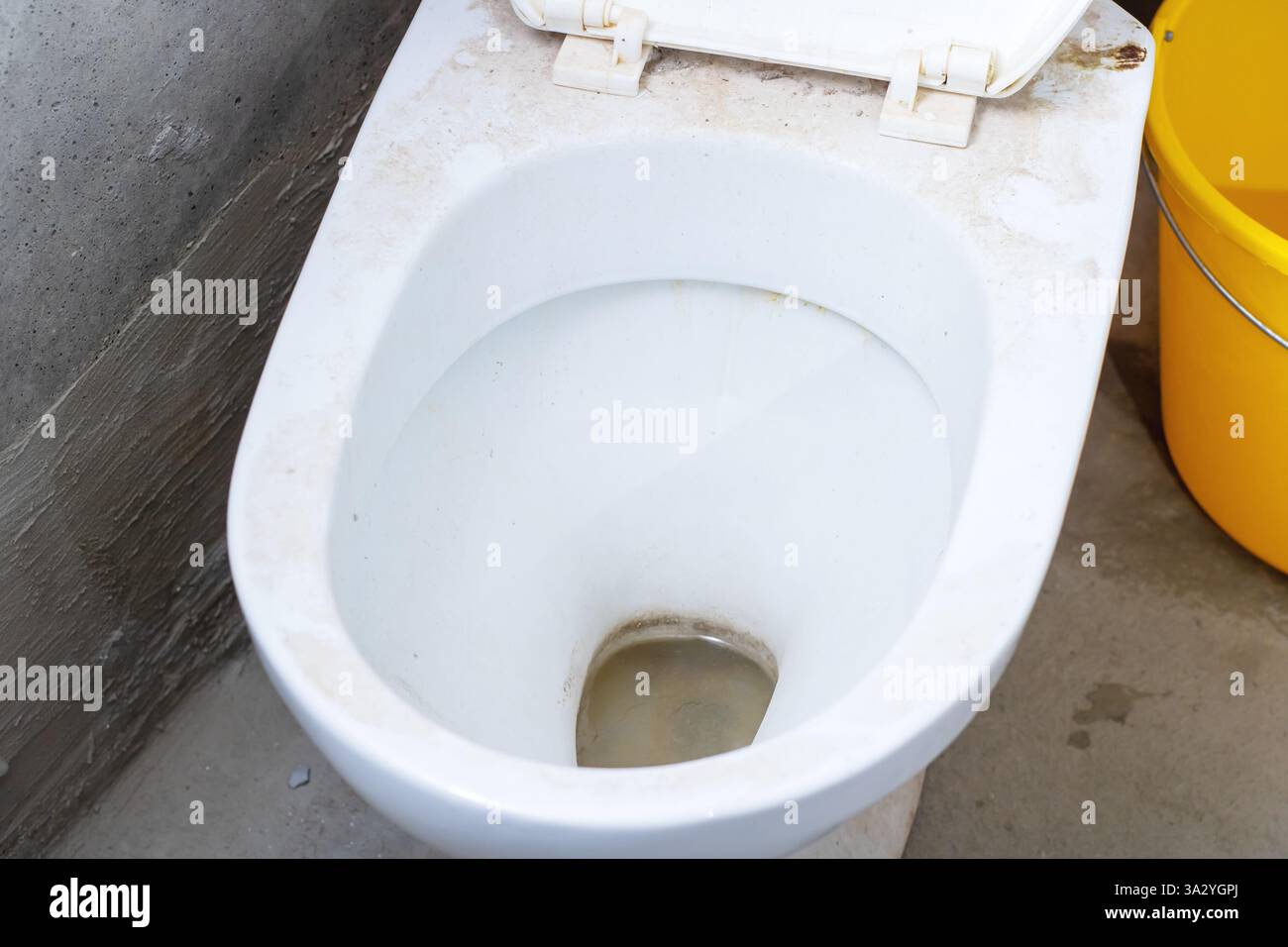 Un gabinetto sporco e poco pulito si trova proprio accanto a un vecchio secchio giallo, che probabilmente viene utilizzato per la pulizia del bagno Foto Stock