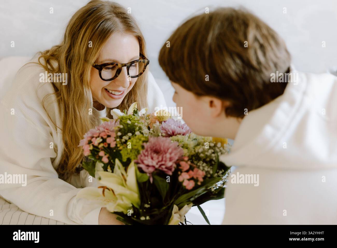 Una madre e un figlio adolescente condividono un momento di cuore con i fiori a casa Foto Stock