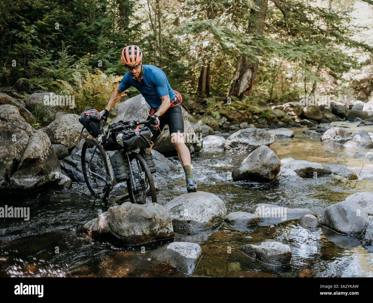 Un ciclista maschile percorre un ruscello mentre fa il bikepacking nella natura selvaggia del Maine Foto Stock