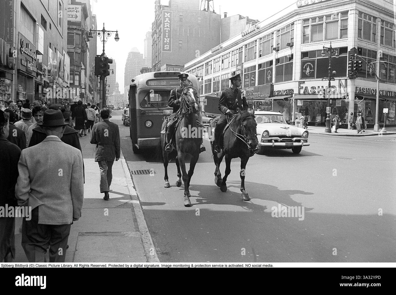New York nel 1959. Una scena di strada con due poliziotti a cavallo in strada. Lo sfondo mostra un ambiente urbano affollato con auto d'epoca ed edifici tipici della New York City della metà del XX secolo. Rif. Roland Palm DV11 *** didascalia locale *** Foto Stock