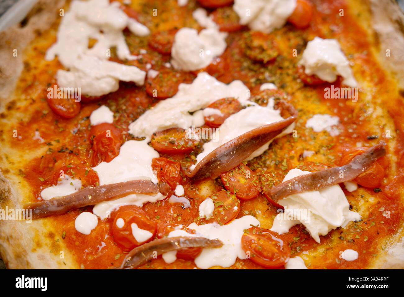 La persona corta e irriconoscibile prepara una pizza gourmet, guarnendo con condimenti freschi come pomodori, acciughe e bambole di formaggio spalmabile. Foto Stock