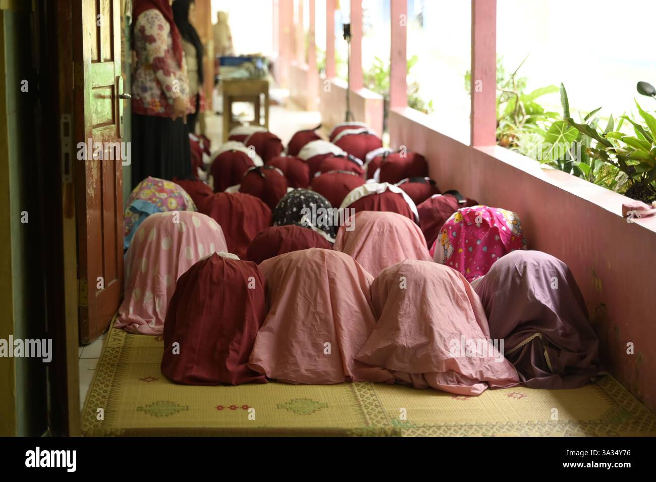 Vista posteriore di donne irriconoscibili vestite con burqa tradizionale e hijab inginocchiate in preghiera, su un pavimento coperto di tappetino. Impegnarsi in un religi o spirituale Foto Stock