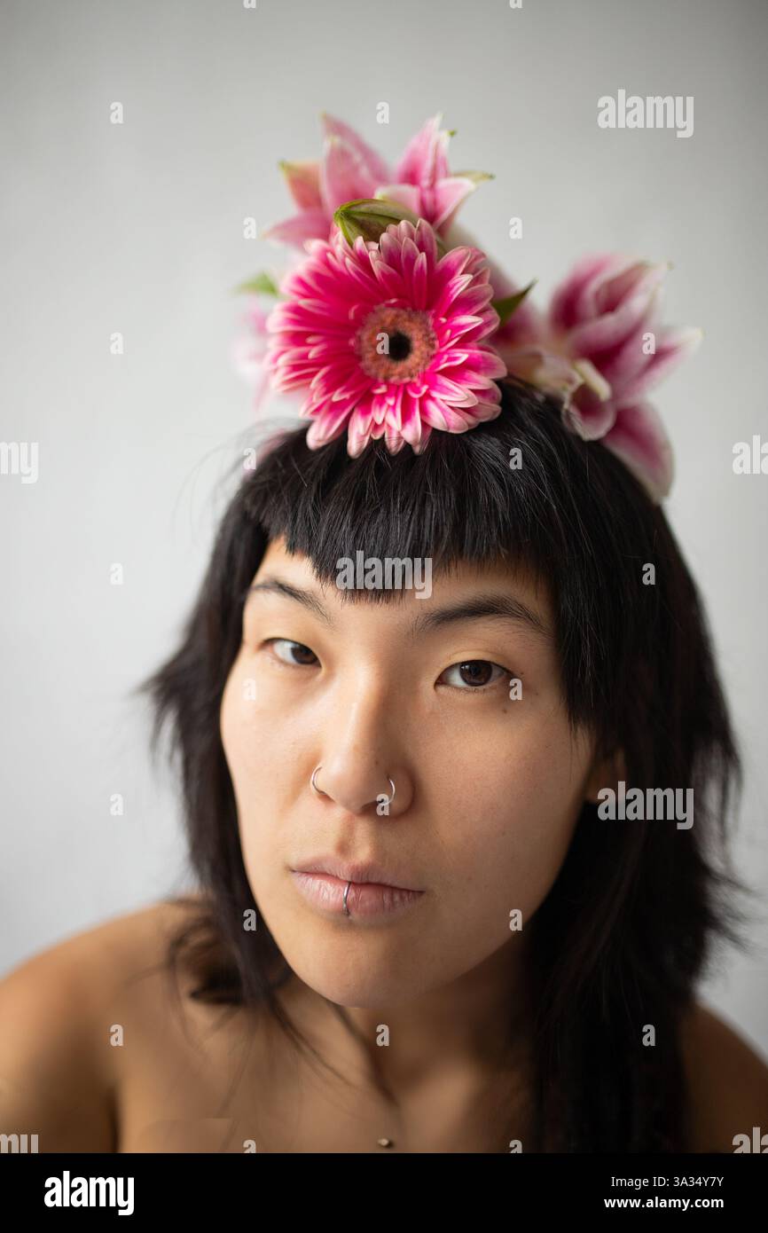 Accattivante ritratto di una donna asiatica che indossa un copricapo floreale, che mostra il suo stile unico con un naso e labbra piercing, su uno sfondo morbido Foto Stock