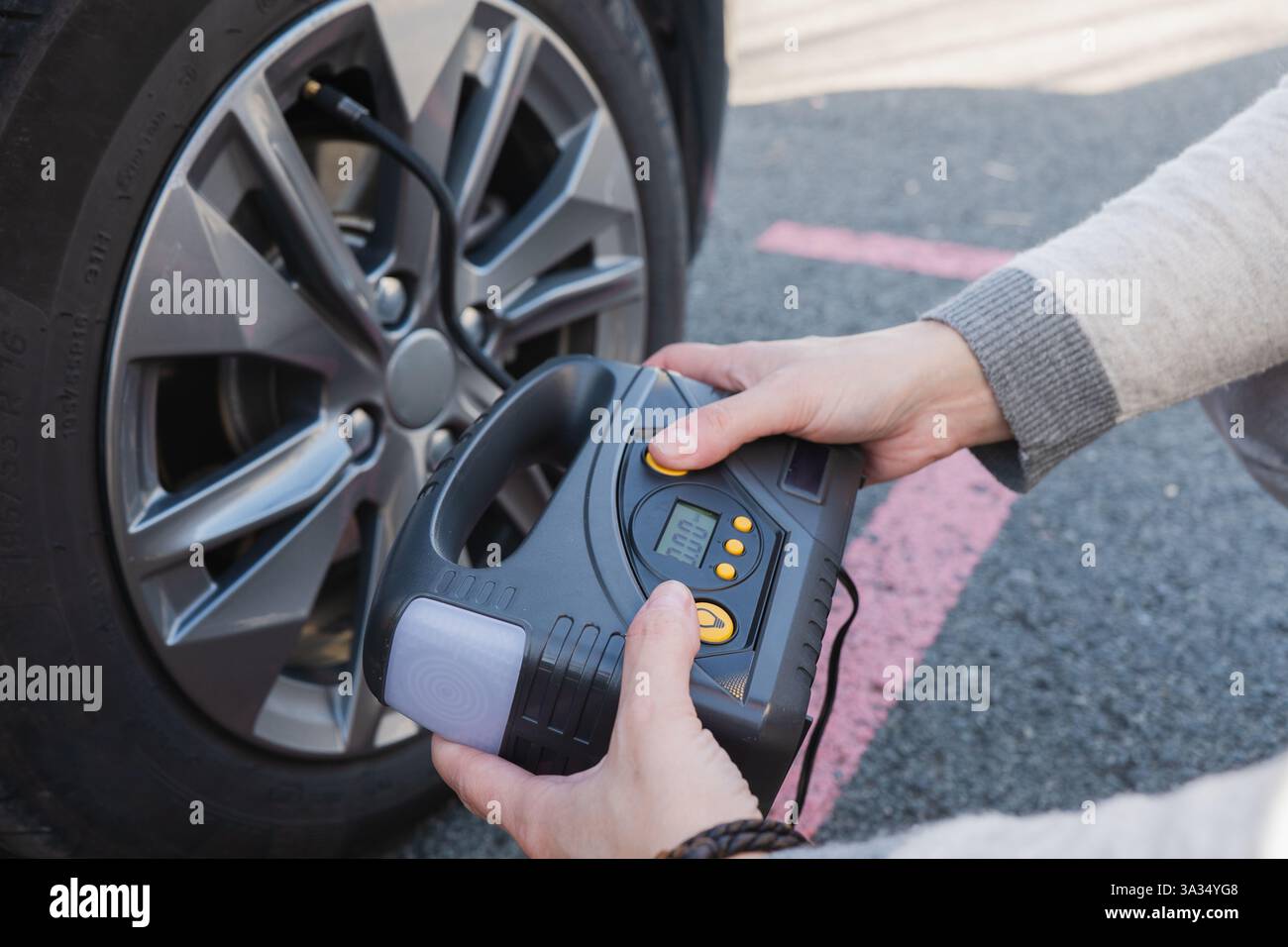 Una persona utilizza un compressore d'aria digitale per controllare e gonfiare lo pneumatico di un'auto elettrica. Il dispositivo compatto visualizza le letture della pressione, garantendo l'optim Foto Stock
