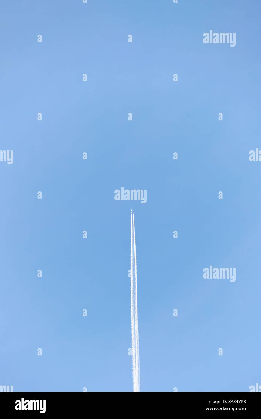 Un aereo lontano lascia una linea diritta su un vasto cielo azzurro, catturando l'essenza del viaggio, della libertà e dell'esplorazione in un'expa aperta Foto Stock