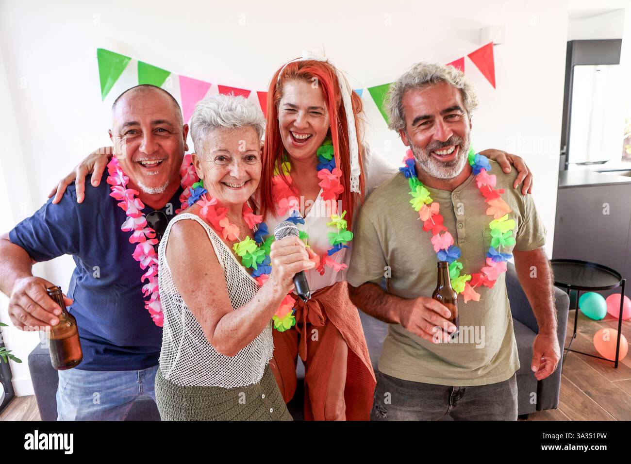 Un gruppo di amici anziani, vestiti di leis colorati, festeggiano con una vivace festa di oltre 50 anni, cantando e divertendosi con un drink. Foto Stock