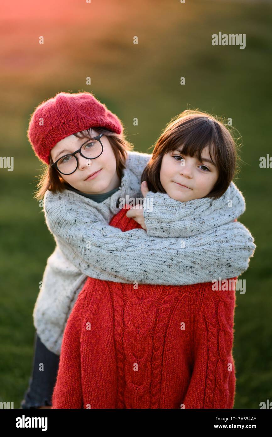 Una ragazza e un fratello condividono un tenero abbraccio, avvolti dal caldo bagliore di un tramonto autunnale, creando una scena emozionante di affetto familiare. Foto Stock
