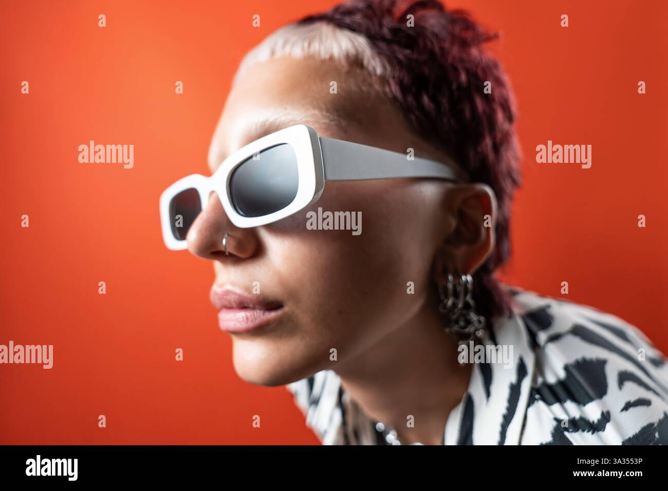 Primo piano di una modella alla moda con occhiali da sole bianchi e abbigliamento con stampa zebra animalier, su uno sfondo arancione vivace. La fotografia flash dello studio Foto Stock