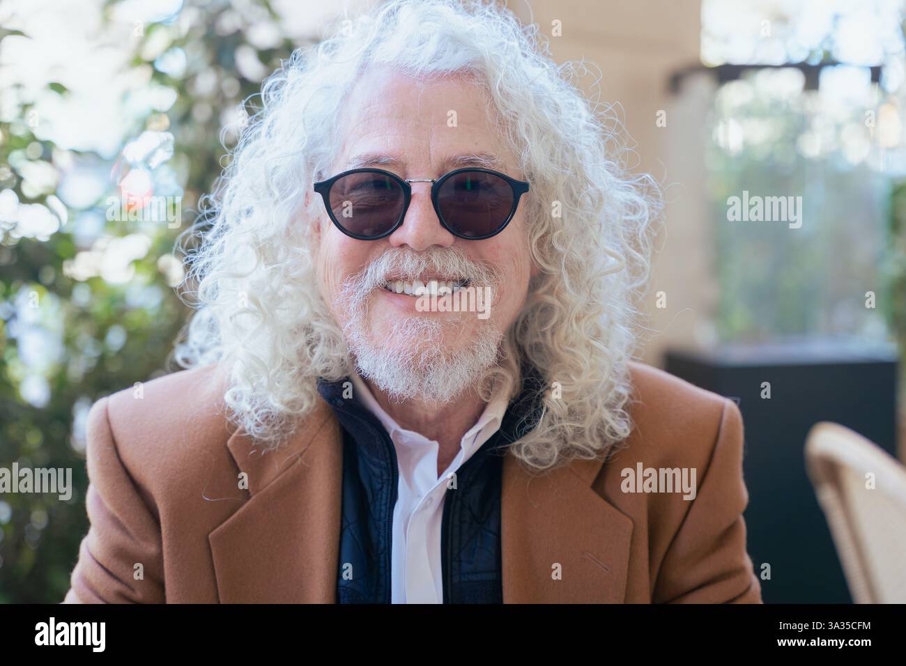 Elegante uomo anziano sorridente alla telecamera in un ambiente urbano all'aperto. Foto Stock