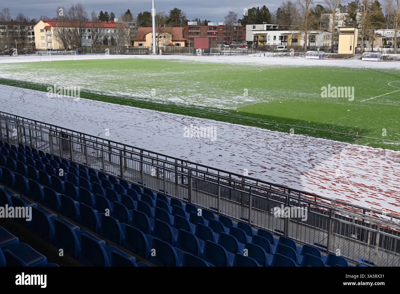 Un campo da calcio parzialmente innevato con erba artificiale, circondato da posti a sedere blu in una struttura sportiva all'aperto. Il freddo e tra Foto Stock