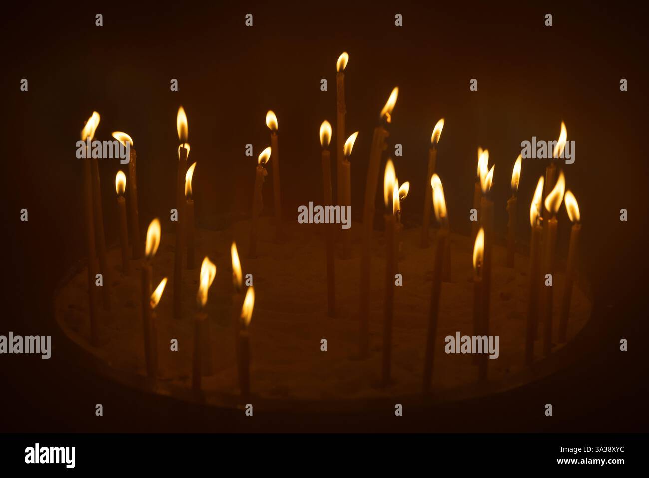 Piccole candele disposte nella sabbia con le loro fiamme che brillano calorosamente su uno sfondo scuro, evocando sentimenti di spiritualità, serenità e riflessione, Foto Stock
