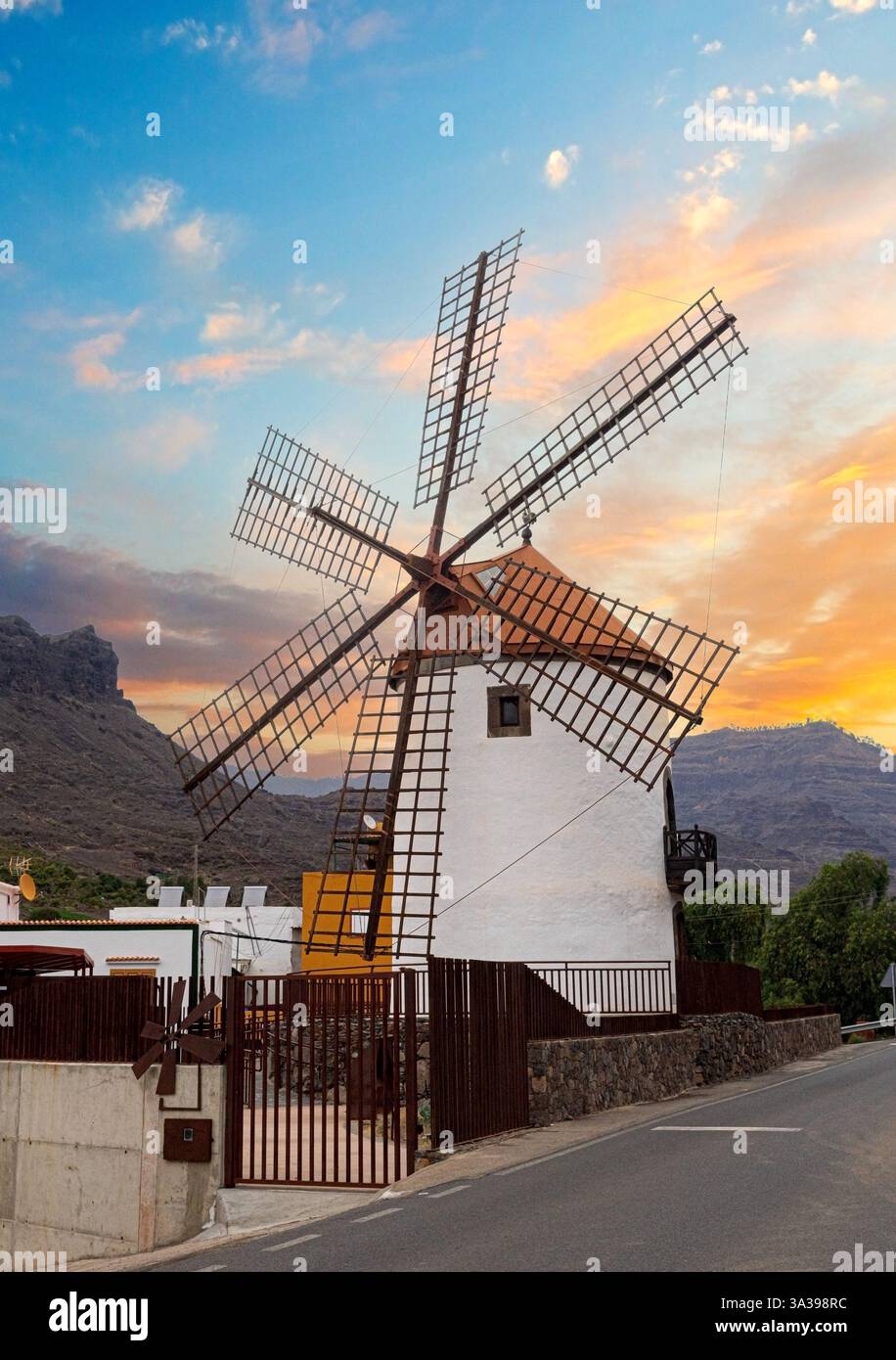Vecchio mulino a vento che si erge alto su un vibrante cielo al tramonto nelle isole canarie, in spagna, che mostra il fascino rurale e l'architettura tradizionale Foto Stock