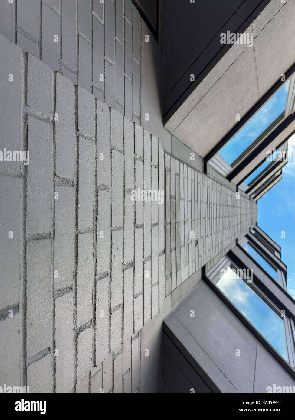 Spettacolare vista verticale di una parete di mattoni chiari con eleganti finestre moderne che riflettono il cielo. La composizione geometrica evidenzia simmetria e trama. Foto Stock