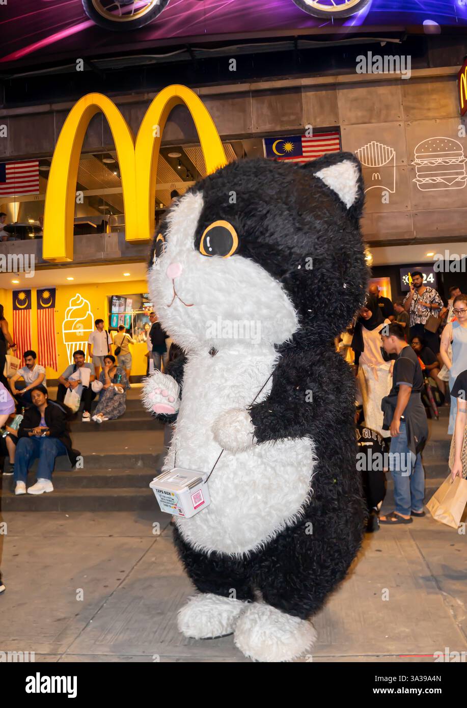 una persona in costume da gatto bianco e nero. Testa tonda con orecchie appuntite e faccia bianca, petto e zampe, cartello McDonalds, Bukit Bintang, Kuala Lumpur, Foto Stock
