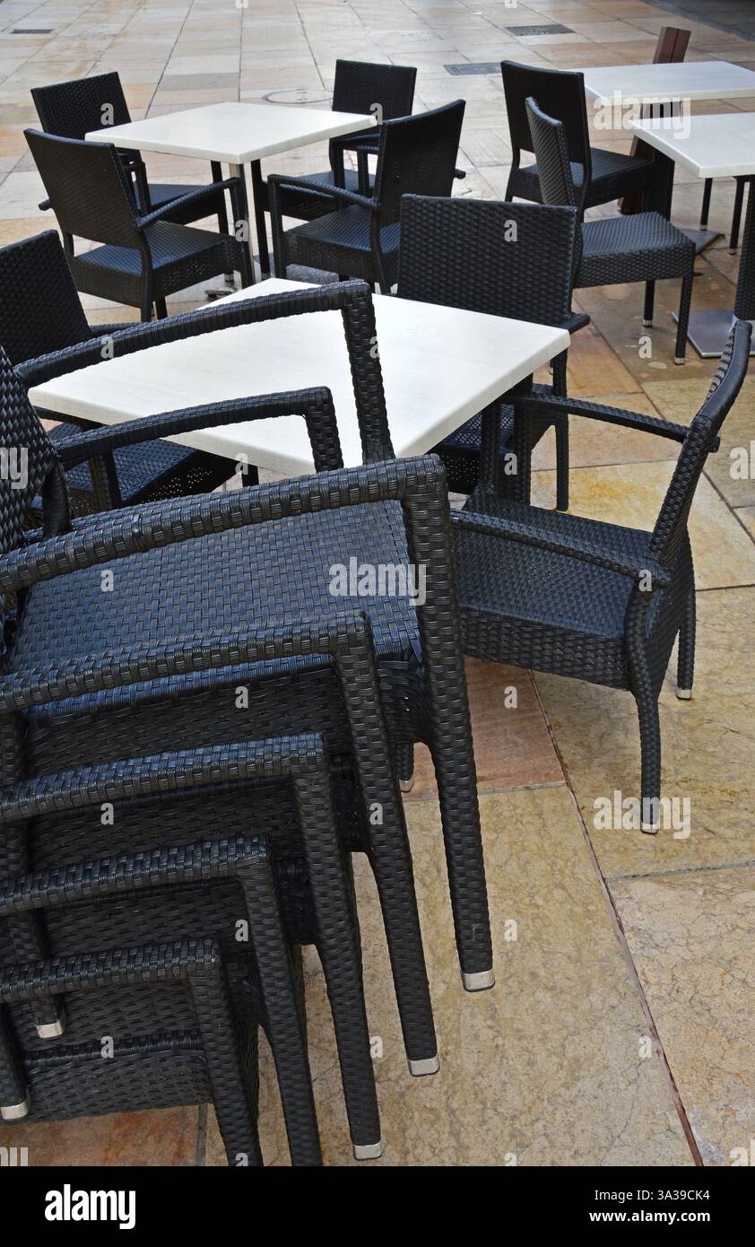 Molte sedie in vimini di plastica e alcuni tavoli bianchi sono impilati sulla strada vicino a un caffè abbandonato Foto Stock