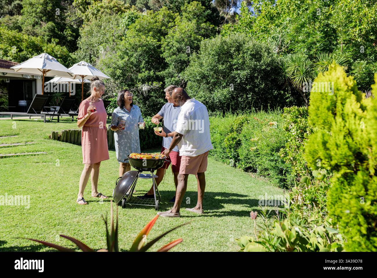 Amici anziani che si godono il barbecue all'aperto in giardino, condividendo cibo e risate insieme Foto Stock