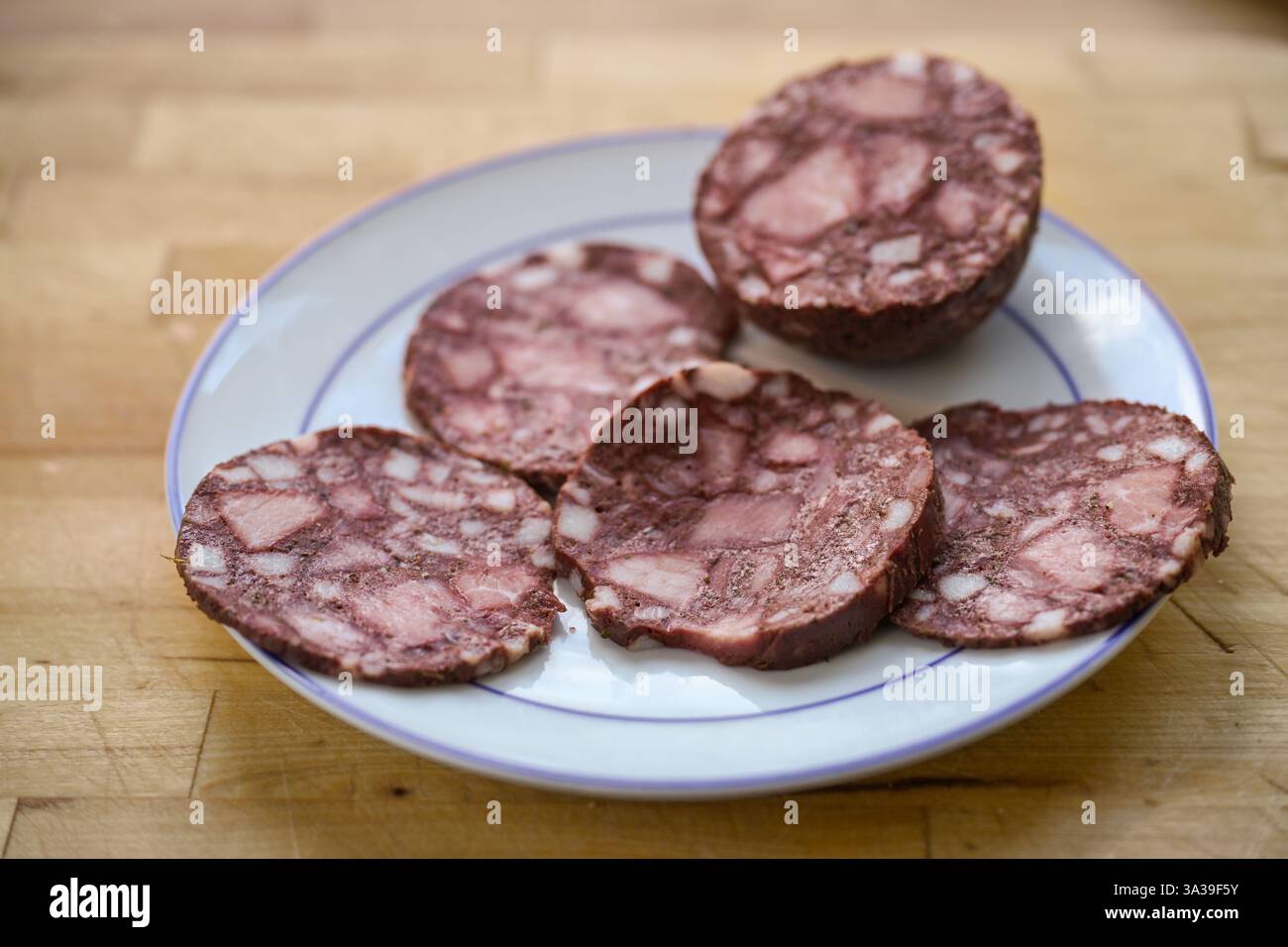 Fette di salsiccia di sangue o budino nero su un piatto e un tavolo in legno rustico, messa a fuoco selezionata, profondità di campo ridotta Foto Stock