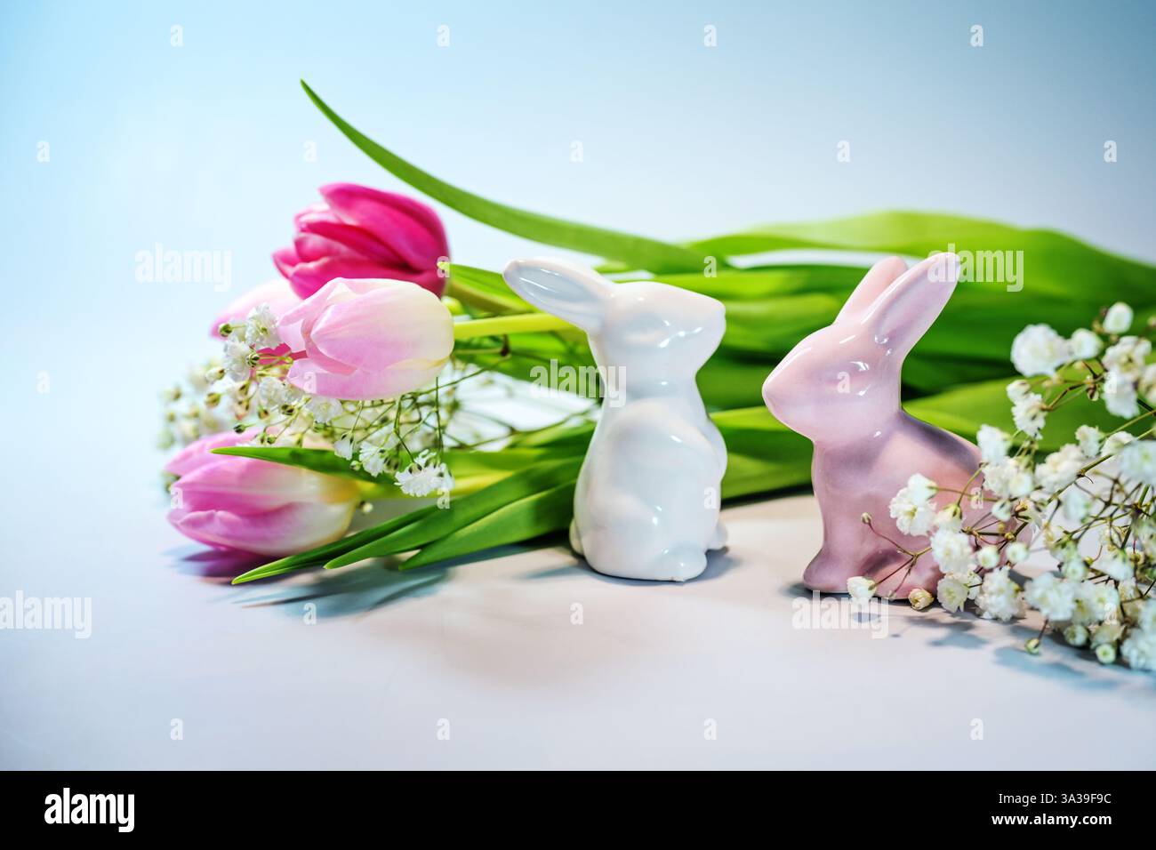 Due coniglietti pasquali in ceramica con un bouquet di tulipani rosa su sfondo azzurro, biglietto d'auguri natalizio, spazio copia, messa a fuoco selezionata Foto Stock