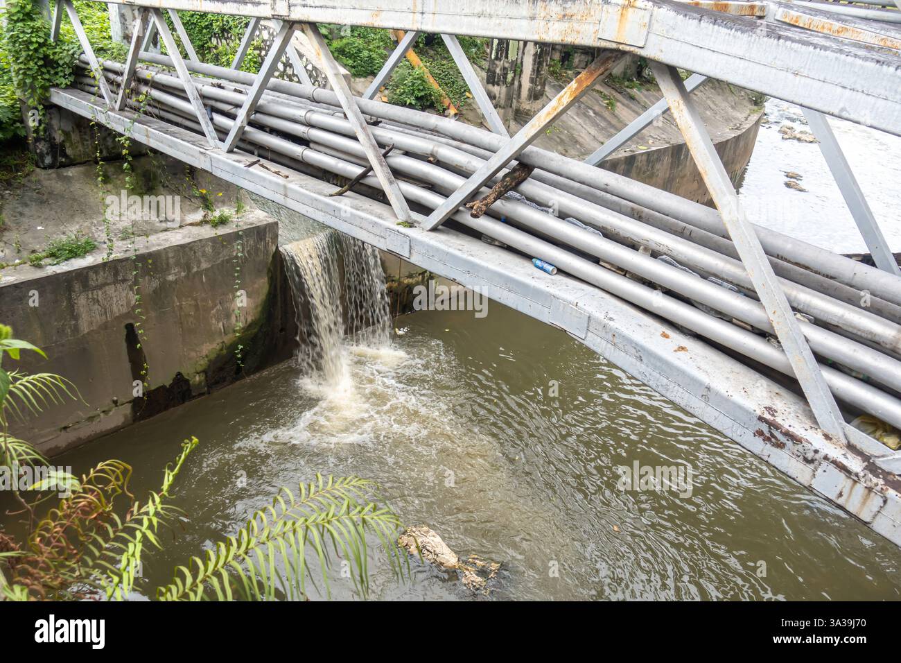 Un ponte di metallo che trasporta diversi tubi su un corso d'acqua, Kuala Lumpur, Malesia, i tubi, probabilmente per servizi come acqua o gas, sono protetti Foto Stock