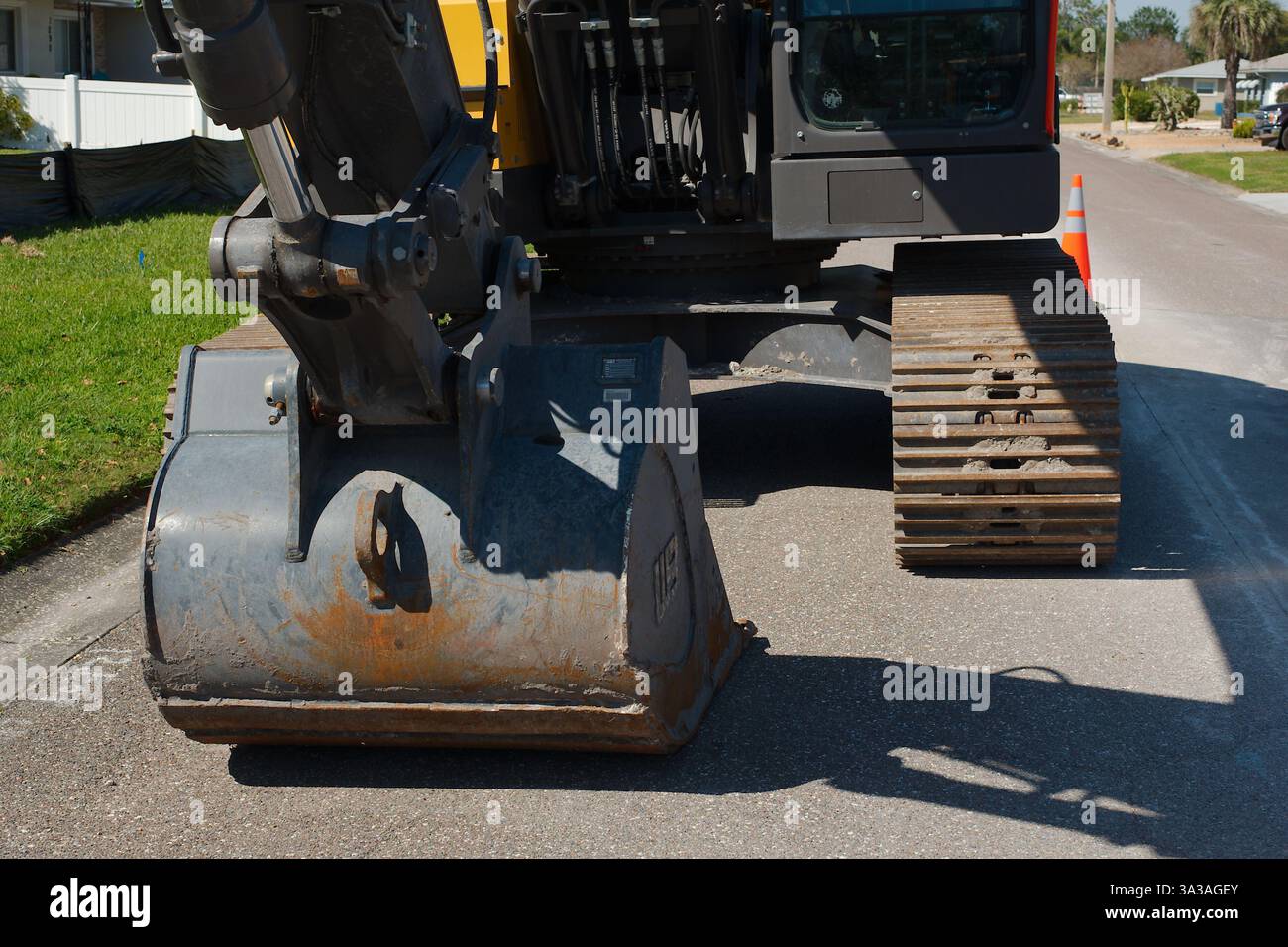Ampia visuale del cingolo e del corpo inferiore di un apripista per escavatore da cantiere con escavatore a benna. Superficie pavimentata coni di traffico in un cantiere per Foto Stock