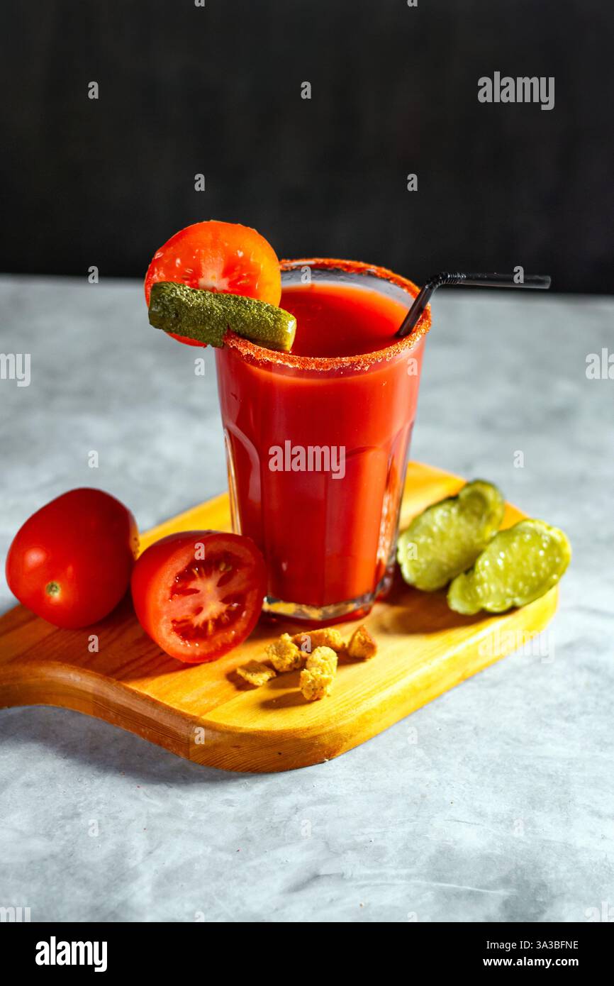 Cocktail agitato di verdure in vetro su sfondo grigio scuro. Cocktail di pomodoro rosso. Servito con pomodori e sottaceti. Menu vegano. Foto Stock