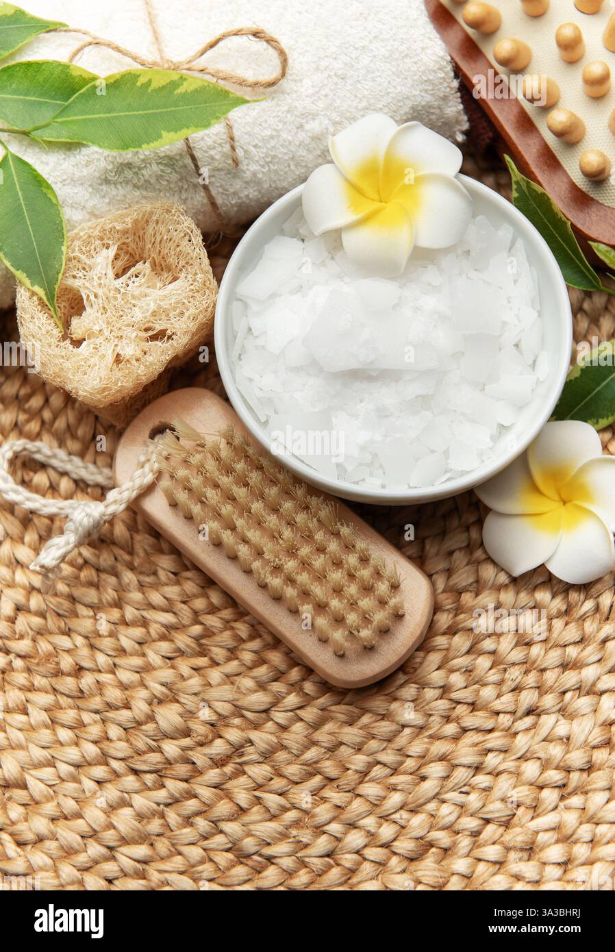 Ambiente benessere con fiocchi di cloruro di magnesio, asciugamano, loofah, pennello e fiori di frangipani Foto Stock