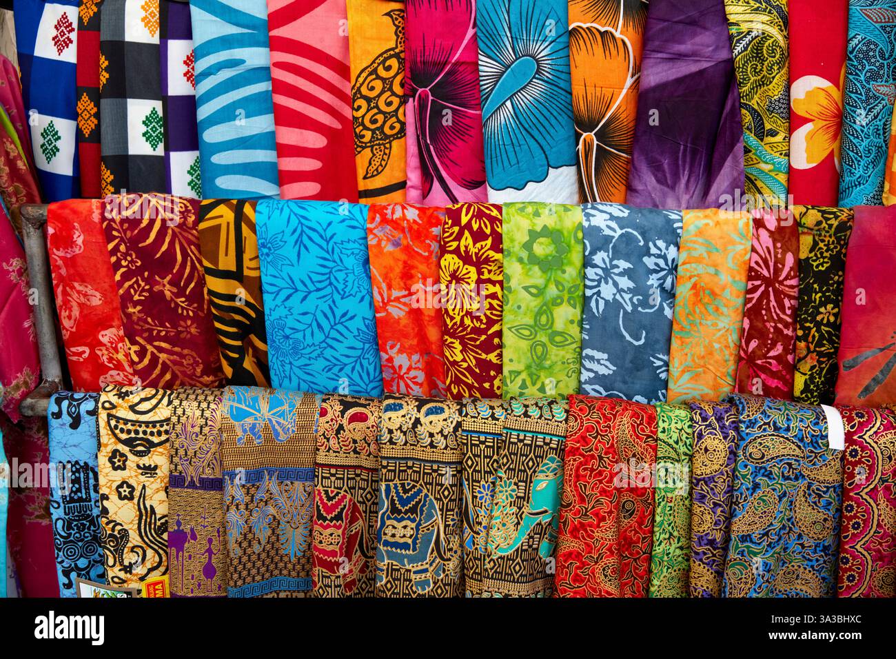 Colorata selezione di sarong piegati in vendita davanti a un negozio di articoli da regalo. Tanah Lot, Bali, Indonesia. Foto Stock