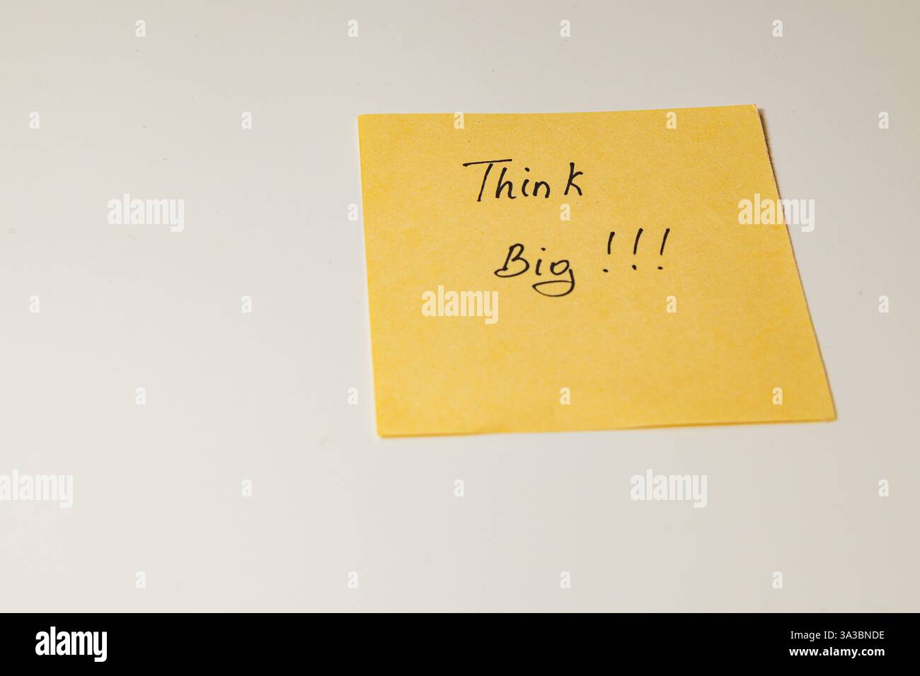 Una nota adesiva gialla con le parole Think Big!!! si trova su un piano di lavoro pulito. Questo serve come incoraggiante promemoria per la creatività e ambi Foto Stock