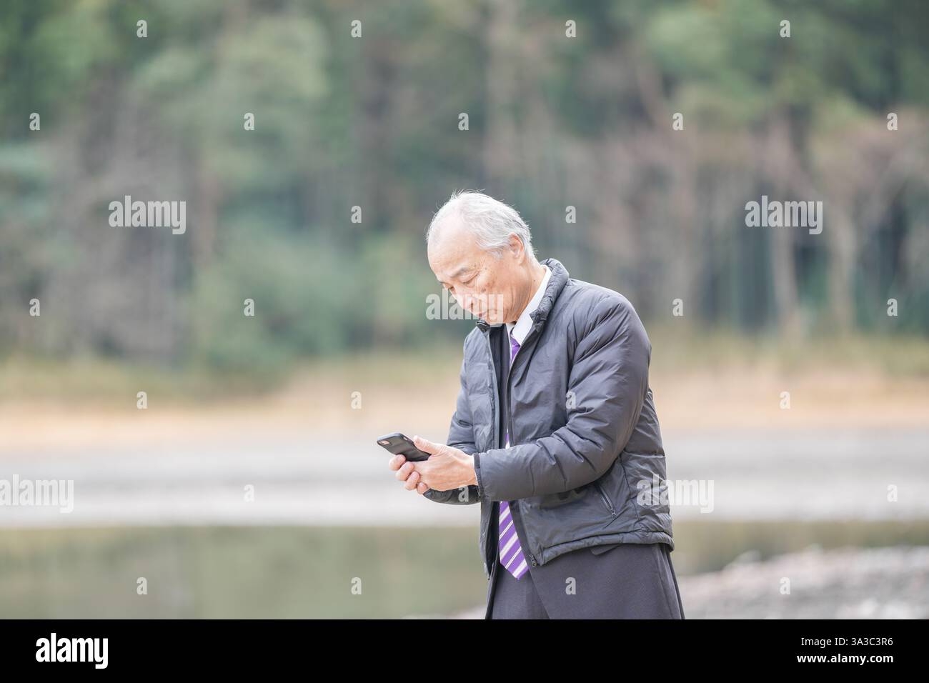 Un laghetto con foresta di bambù in un giorno primaverile di mezzogiorno in Giappone con molta vegetazione. Un uomo giapponese alla fine degli anni '70 è in piedi con un vestito e una piumino. Lui Foto Stock