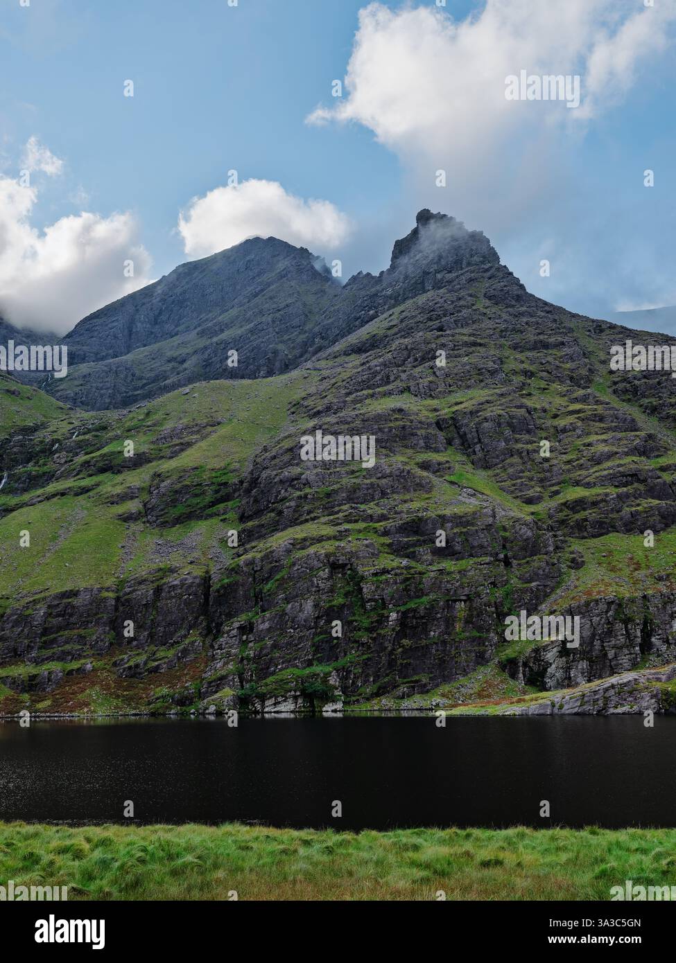 Lough Gouragh mette in mostra lo splendido paesaggio naturale dell'Irlanda, incorniciato da aspre montagne e lussureggiante vegetazione sotto un cielo parzialmente nuvoloso. Foto Stock