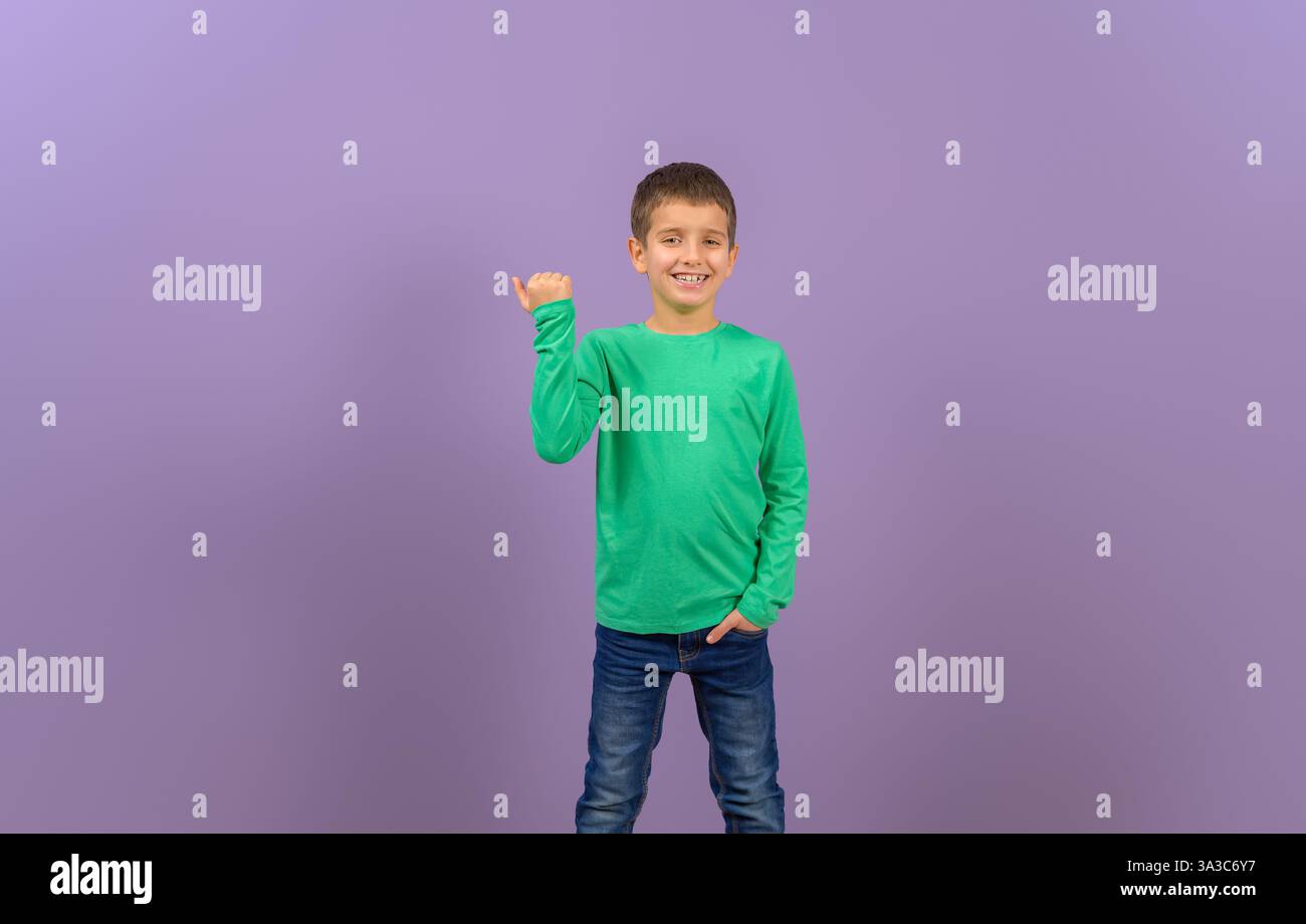 Ritratto di uno scolaro carino con la mano in tasca sorridente e pugno tremante su sfondo viola isolato Foto Stock