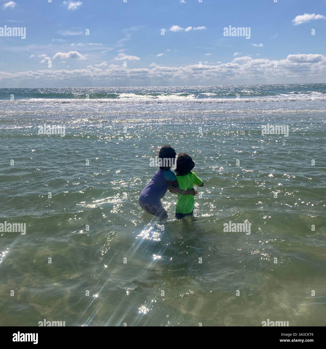 I bambini si aggrappano l'un l'altro mentre si immergono nell'oceano a Anna Maria Island, Florida, Stati Uniti Foto Stock