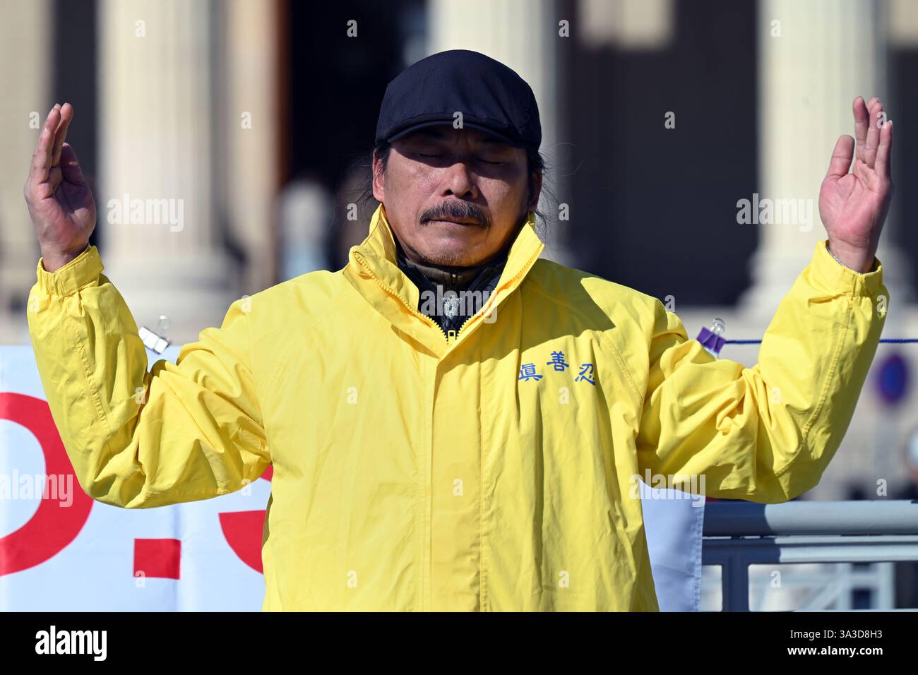 Piazza degli Eroi, Budapest, Ungheria - 2 marzo 2025: Manifestante del Falun Gong maschile con giacca gialla che medita in posizione eretta del Falun Foto Stock