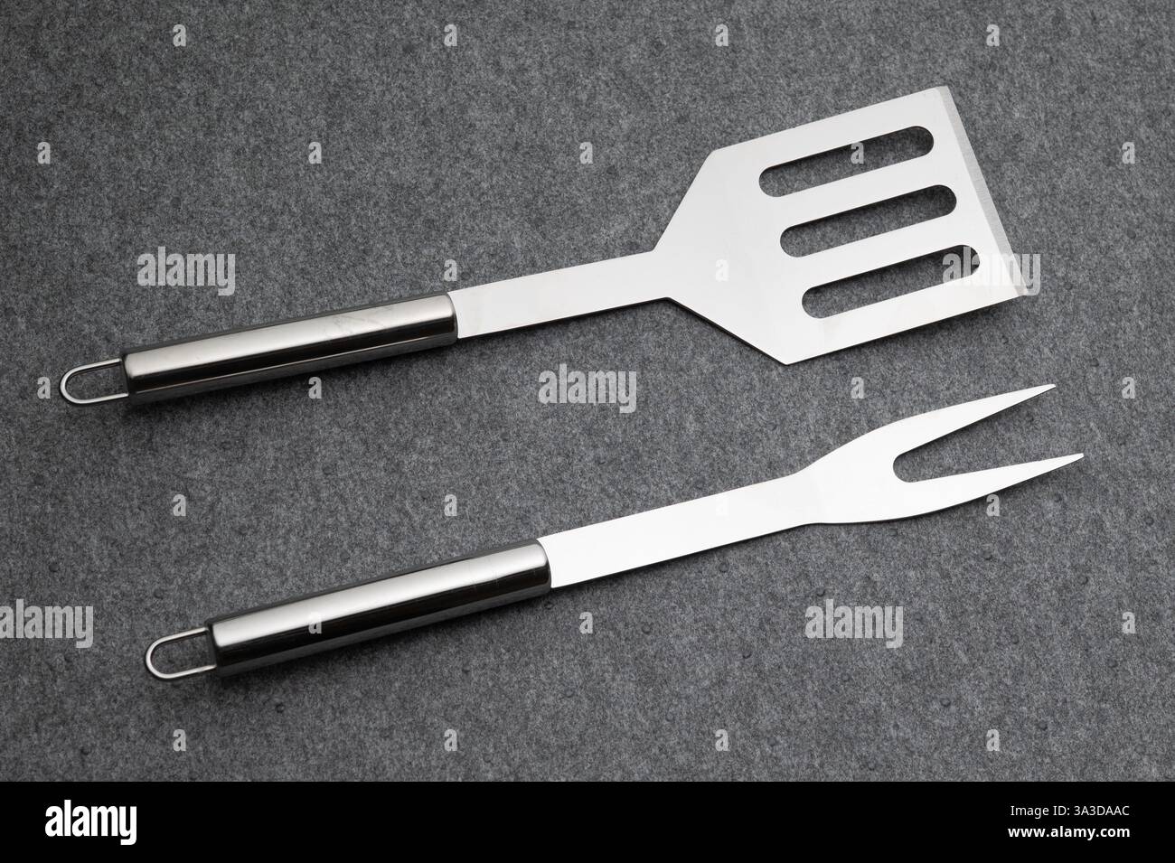 , Deutschland, 15.03.2025, Hochwertiges Edelstahl-Grillbesteck, bestehend aus Grillzange, Grillgabel und Grillwender, auf grauem Hintergrund. Perfekt Foto Stock