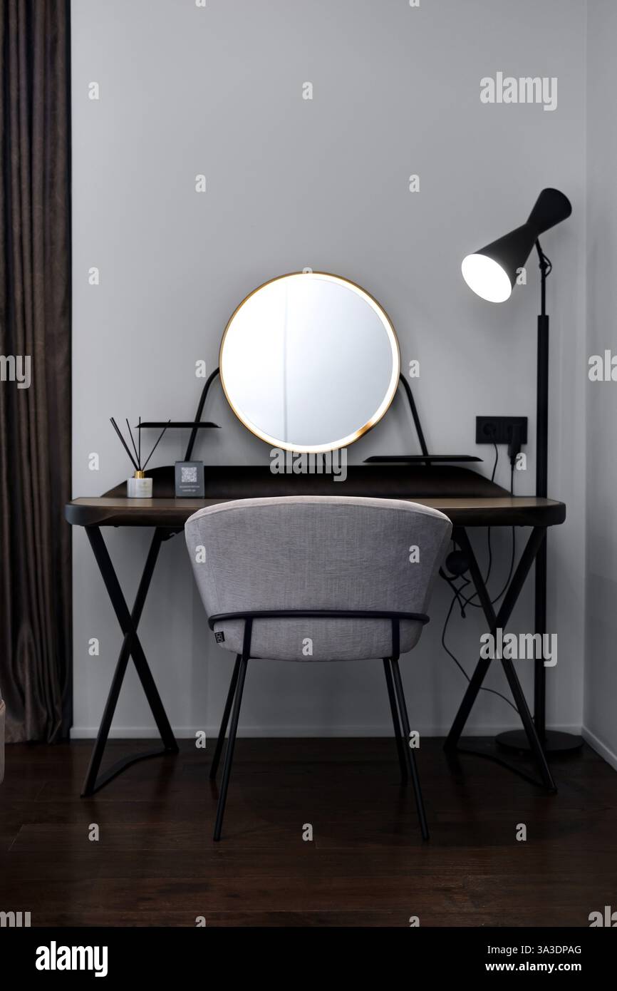 Moderna scrivania con specchio ed elegante sedia grigia in camera minimalista Foto Stock